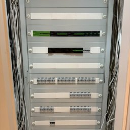 IE SOLUTIONS SPÓŁKA Z OGRANICZONĄ ODPOWIEDZIALNOŚCIĄ - Szara szafa rozdzielcza z licznymi kablami po bokach, zawierająca moduły z oznaczeniami A1 do A31 i urządzeniami elektronicznymi, zamontowana wewnątrz pomieszczenia.