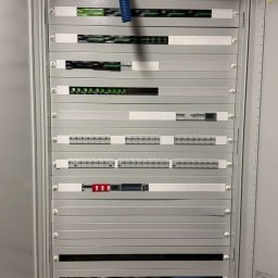 IE SOLUTIONS SPÓŁKA Z OGRANICZONĄ ODPOWIEDZIALNOŚCIĄ - Wnętrze rozdzielnicy elektrycznej z modułami, zabezpieczeniami i przewodami, widoczne elementy sterujące i złącza, całość w szarej obudowie.