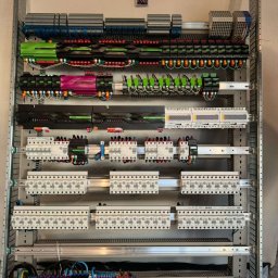 IE SOLUTIONS SPÓŁKA Z OGRANICZONĄ ODPOWIEDZIALNOŚCIĄ - Rozdzielnica elektryczna z modułami sterującymi, zabezpieczeniami i okablowaniem, widok z bliska ukazujący szczegóły połączeń i komponentów w szafie sterowniczej.