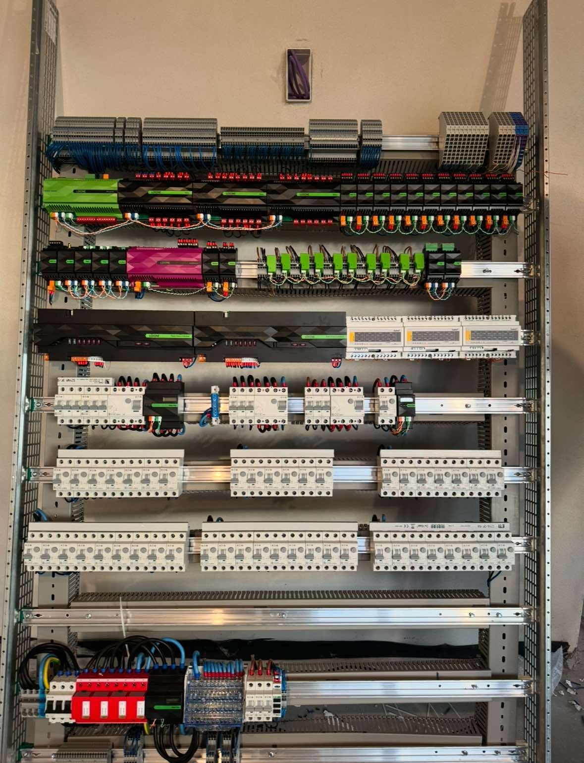 Rozdzielnica elektryczna z modułami sterującymi, zabezpieczeniami i okablowaniem, widok z bliska ukazujący szczegóły połączeń i komponentów w szafie sterowniczej.