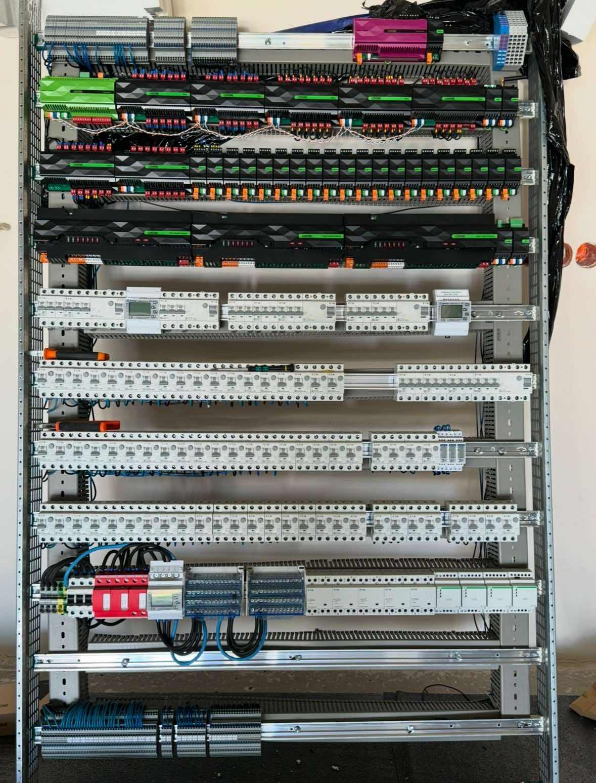Rozdzielnica elektryczna z modułami sterującymi, zabezpieczeniami i okablowaniem, widok od frontu, różnokolorowe komponenty.