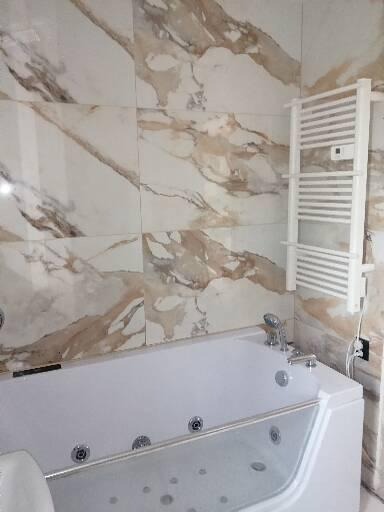 Biała wanna z hydromasażem w łazience z marmurowymi płytkami i grzejnikiem drabinkowym.