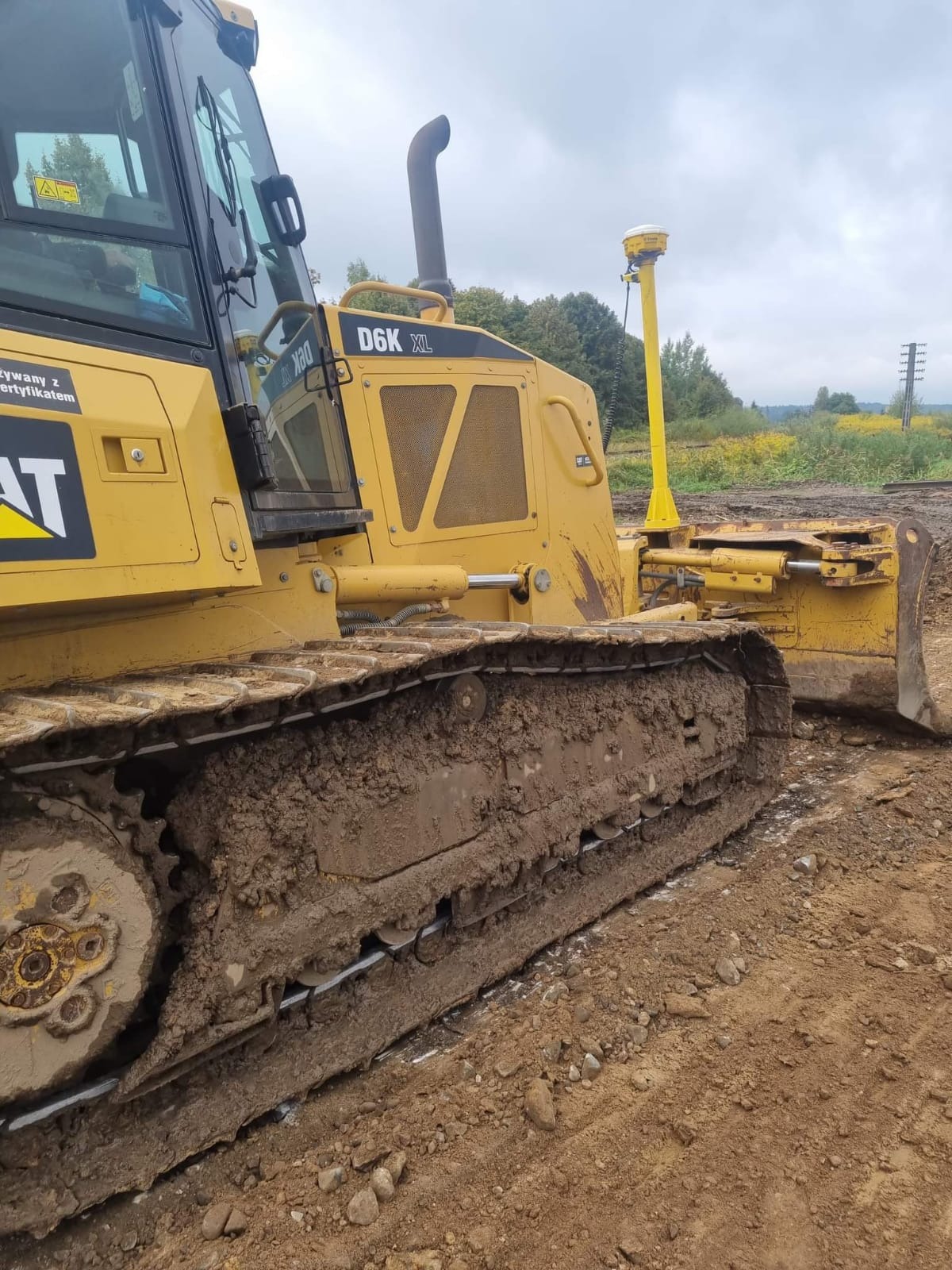 Żółta spycharka CAT D6K XL z systemem GPS 3D, ubrudzona ziemią, stoi na placu budowy.