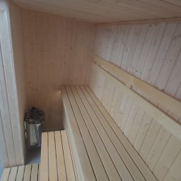 MAS-KOMINKI Krzysztof Sobczyk - Wnętrze nowej, jasnej sauny z drewnianymi ławkami w Legionowie, z widocznym piecem na kamienie.