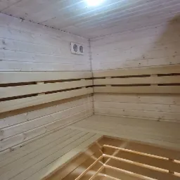 Wnętrze sauny wykończone jasnym drewnem, z widocznymi ławkami, panelami ściennymi i systemem wentylacji.