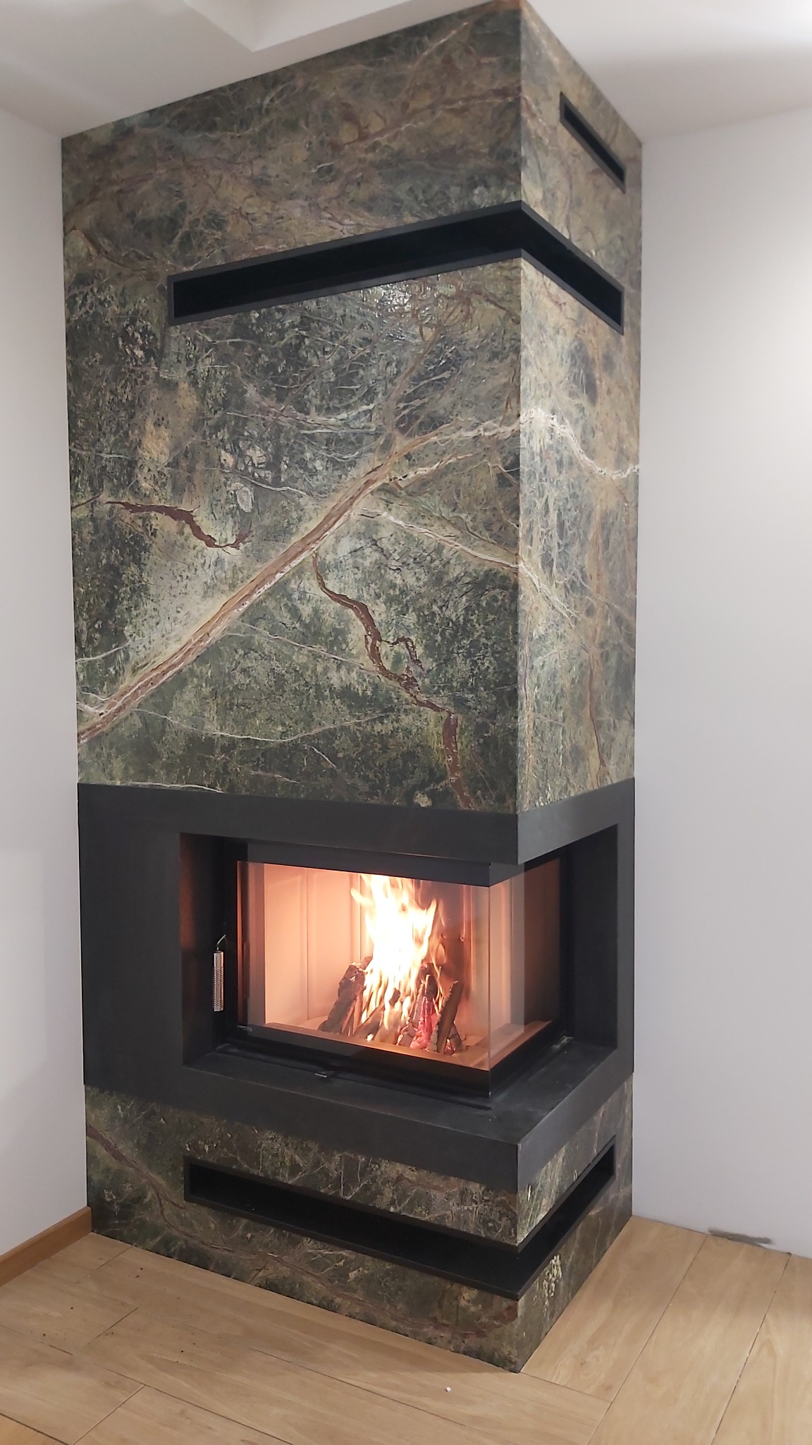 Nowoczesny kominek narożny, obudowa wykonana z kamienia Forest Green oraz Nero