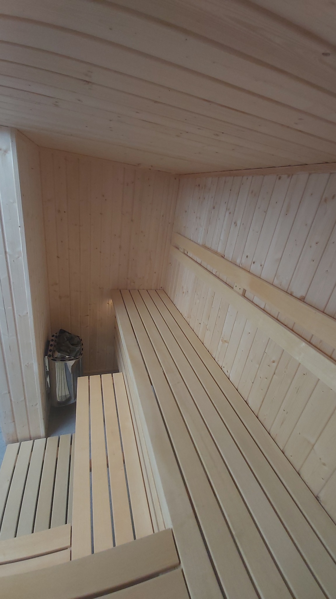 Wnętrze nowej, jasnej sauny z drewnianymi ławkami w Legionowie, z widocznym piecem na kamienie.