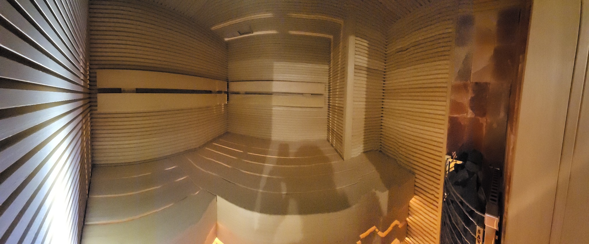 Wnętrze sauny wykończone jasnym drewnem, widoczne ławki i oświetlenie, perspektywa szerokokątna.
