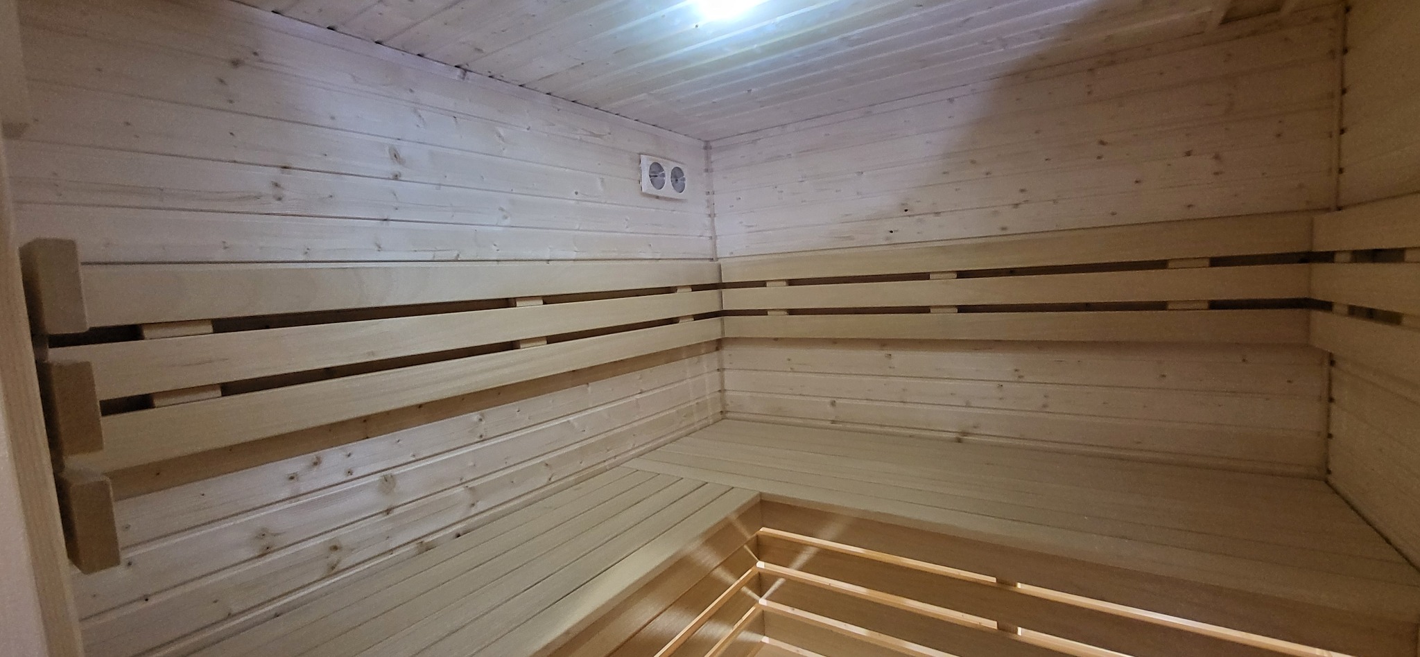 Wnętrze sauny wykończone jasnym drewnem, z widocznymi ławkami, panelami ściennymi i systemem wentylacji.