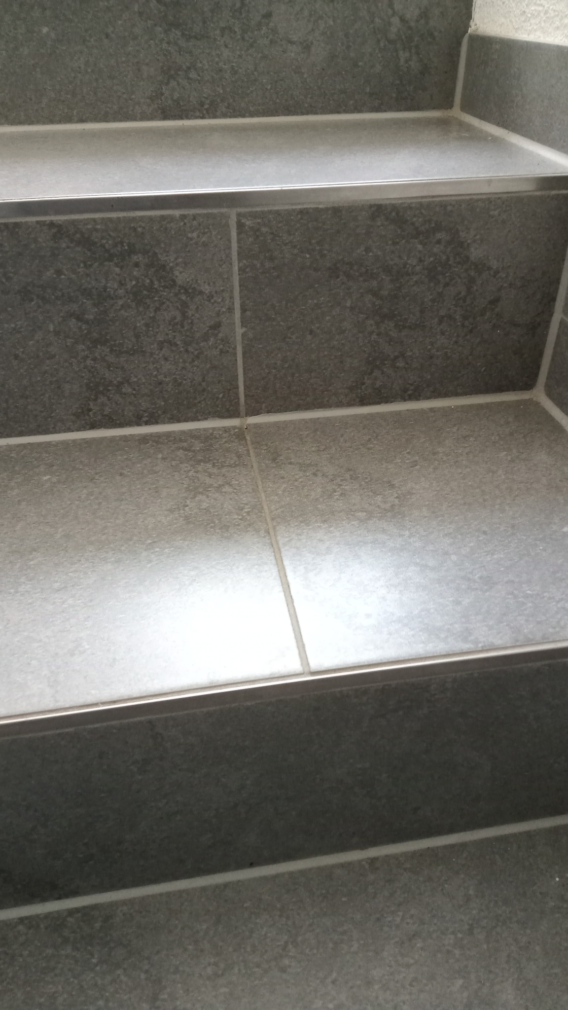 Szare płytki ceramiczne na schodach z metalowymi listwami krawędziowymi, widok z bliska.