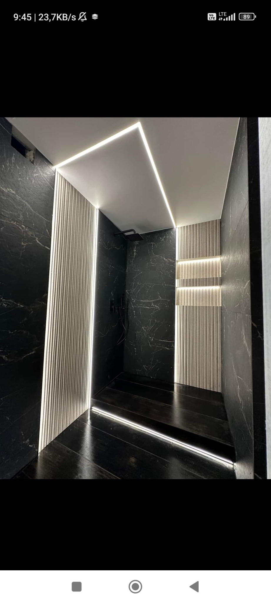 Nowoczesna łazienka z czarnymi marmurowymi ścianami, podświetlanymi panelami ściennymi i oświetleniem LED na suficie i podłodze, tworzącymi geometryczne wzory.