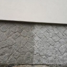 Fragment ściany z kamienia elewacyjnego, z widoczną różnicą w czystości między umytą a nieumytą częścią. Górna część ściany pomalowana na biało.