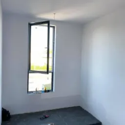 Wnętrze w trakcie prac: świeżo pomalowane ściany na biało, czarna marmurowa podłoga i schody, otwarte okno z widokiem na zieleń, narzędzia i węże na podłodze.