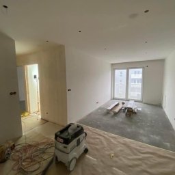 Wykończenia wnętrz Krzyś-Art Krzysztof Włodarczyk - Pokój w trakcie prac wykończeniowych: ściany po gładzi, przygotowane do malowania, widoczny odkurzacz przemysłowy Festool, zabezpieczona podłoga i okno balkonowe.