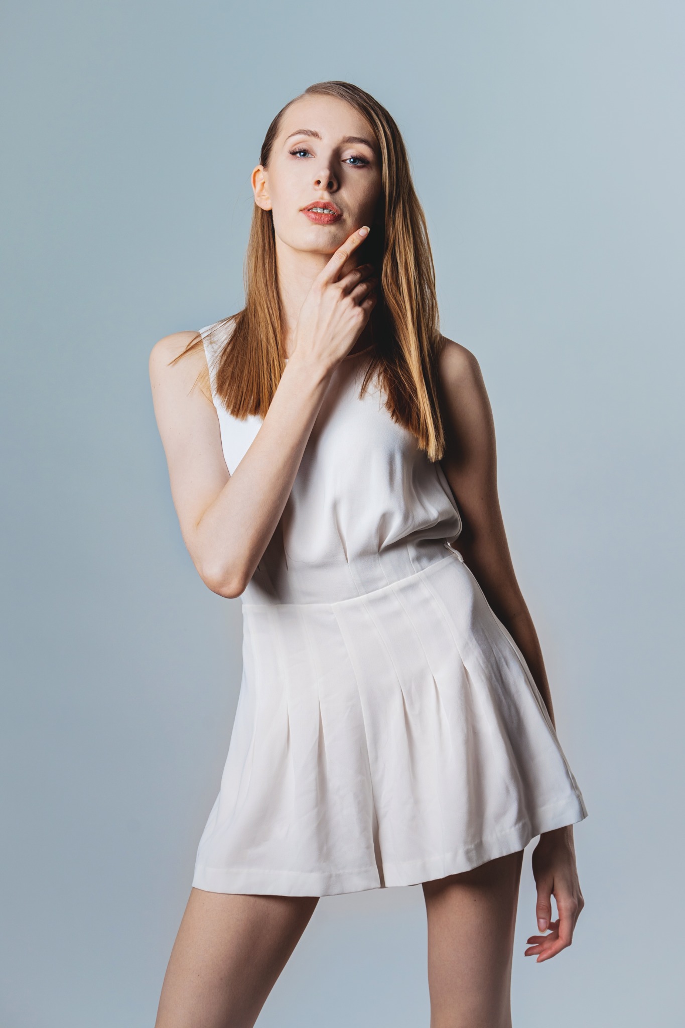 Portret kobiety z jasnymi włosami i subtelnym podkreśleniem ust, pozującej w białym komplecie na jednolitym tle.