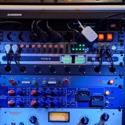 Adam Kruk - Sprzęt studyjny: Rząd profesjonalnych urządzeń audio z pokrętłami, miernikami VU i podświetleniem, tworzących zaawansowany system do nagrywania i miksowania dźwięku.