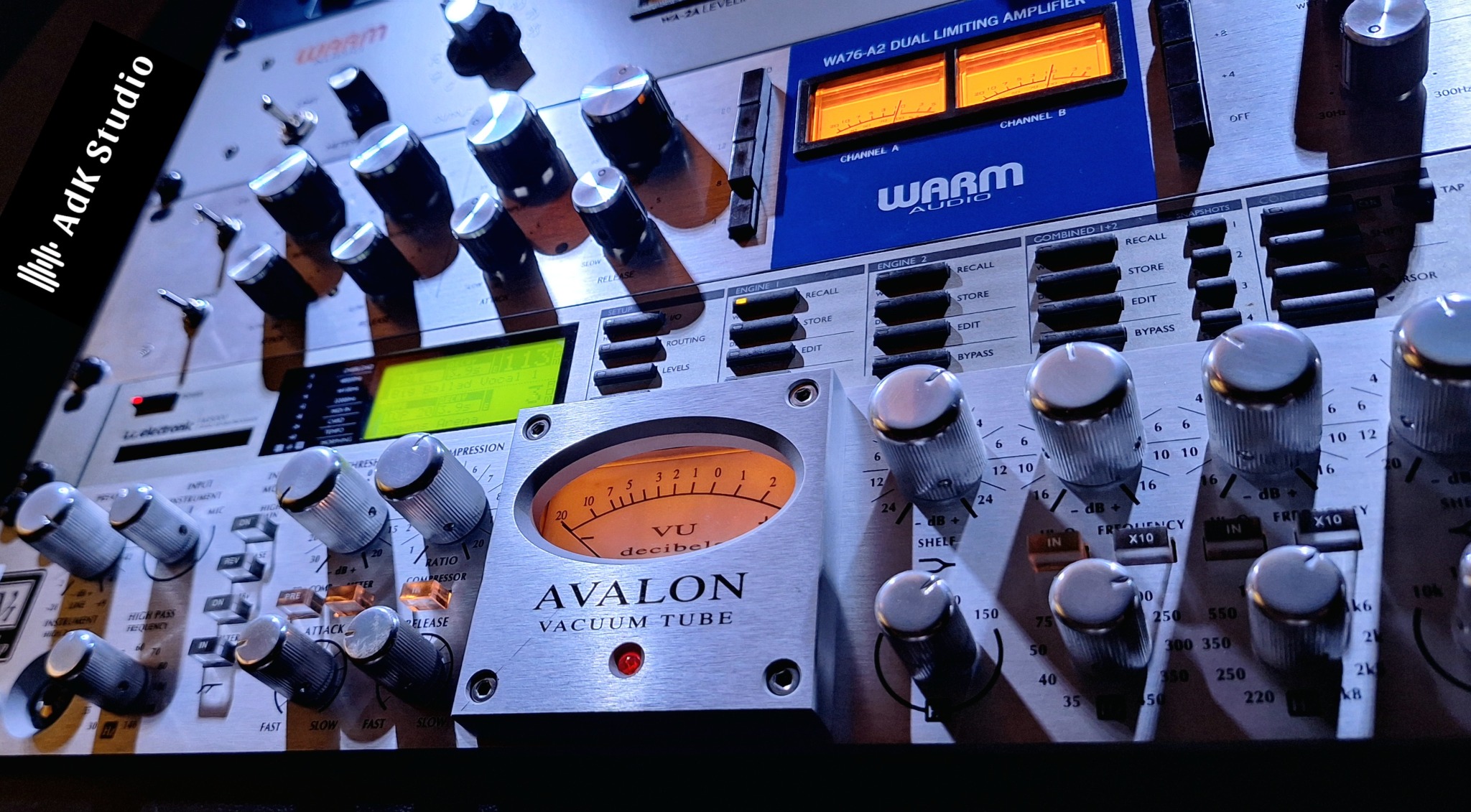 Panel mikserski z pokrętłami i wskaźnikami VU, marki Avalon i Warm Audio, oświetlony studyjnym światłem. Sprzęt audio w zbliżeniu, detale regulacji dźwięku.