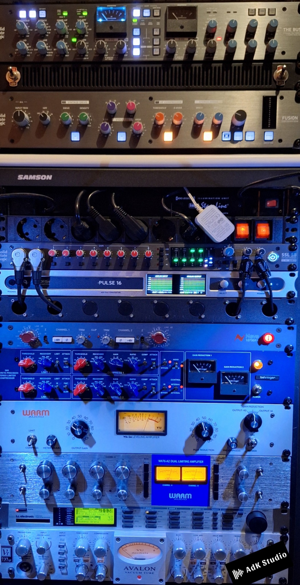 Sprzęt studyjny: Rząd profesjonalnych urządzeń audio z pokrętłami, miernikami VU i podświetleniem, tworzących zaawansowany system do nagrywania i miksowania dźwięku.