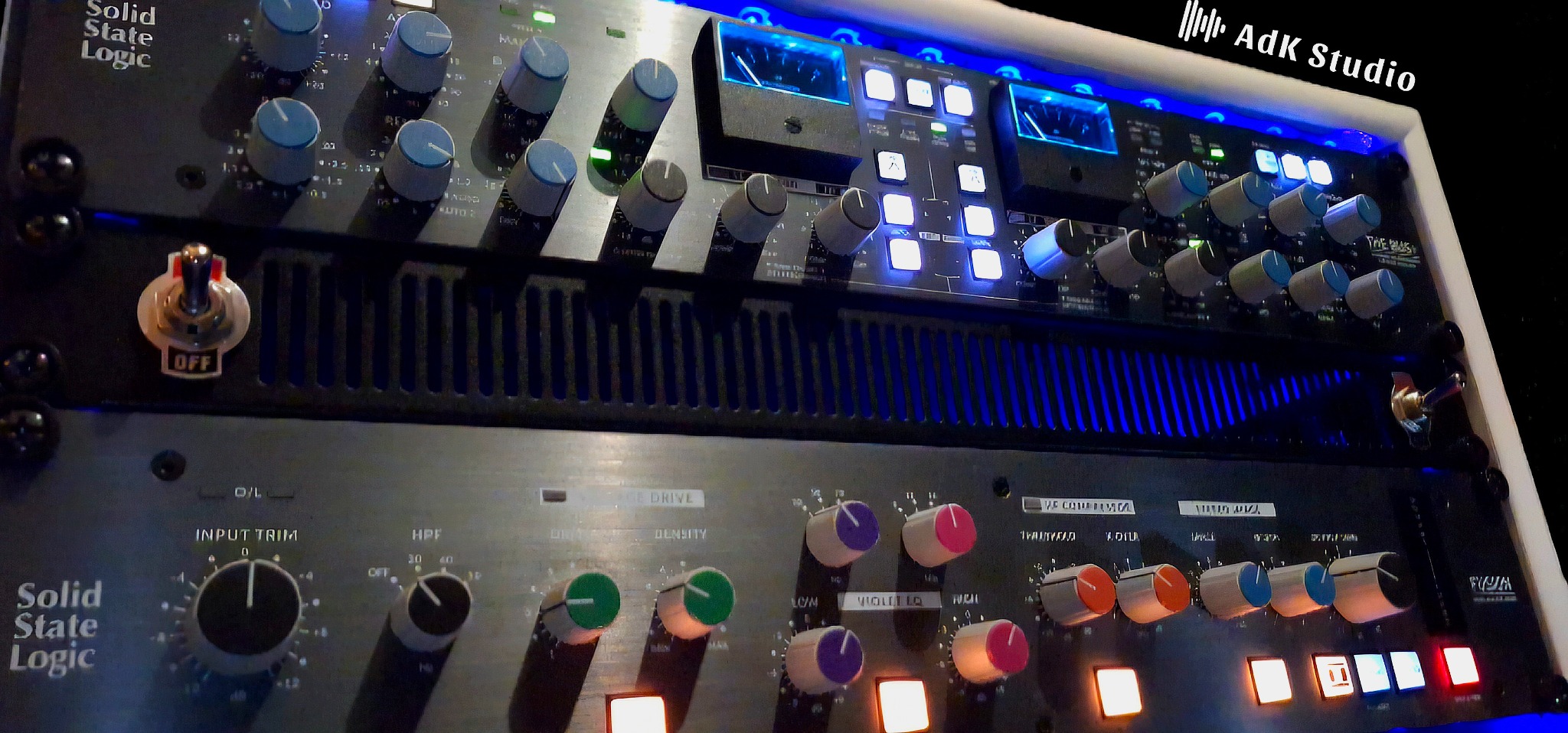 Profesjonalny sprzęt audio Solid State Logic z podświetleniem LED w studio nagrań. Widoczne liczne pokrętła i przełączniki. Logo AdK Studio w prawym górnym rogu.