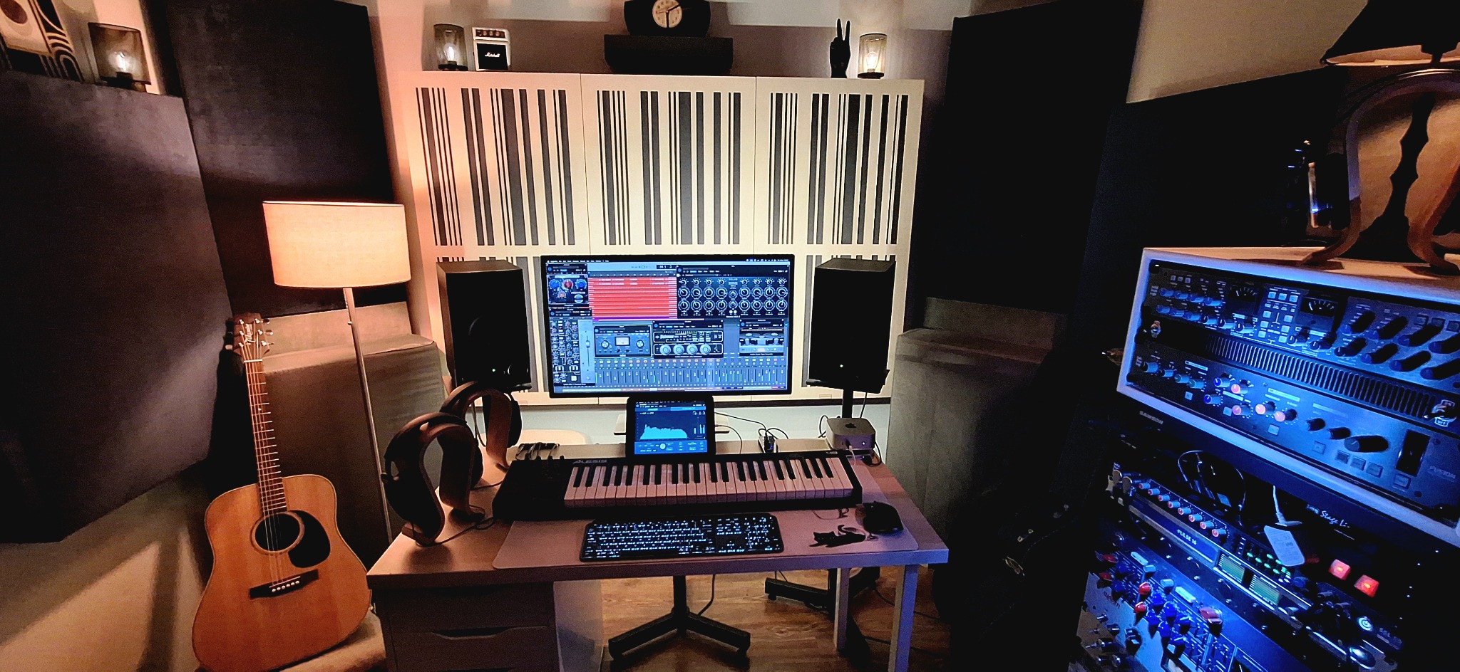Profesjonalne studio nagrań z gitarą akustyczną, klawiaturą, słuchawkami i ekranem z oprogramowaniem do edycji dźwięku. Panele akustyczne na ścianach.