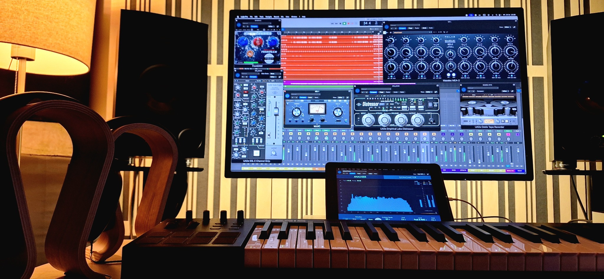 Aranżacja studia nagrań: klawiatura MIDI, tablet z analizatorem dźwięku, monitor z oprogramowaniem DAW, lampa i panele akustyczne w tle. Ciepłe oświetlenie.