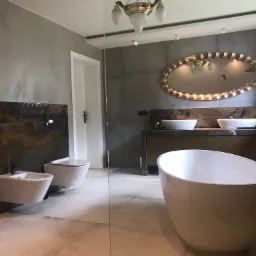 Elegancka łazienka w odcieniach szarości i beżu z wolnostojącą wanną, umywalkami nablatowymi, owalnym lustrem w złotej ramie i złotym żyrandolem w stylu retro.