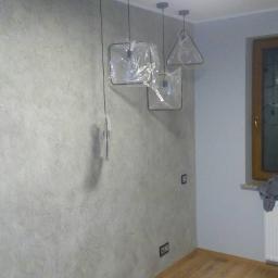 FirmBud - Pokój po remoncie z nową teksturą na ścianie, drewnianą podłogą i trzema nowoczesnymi lampami wiszącymi w plastikowych osłonach ochronnych.