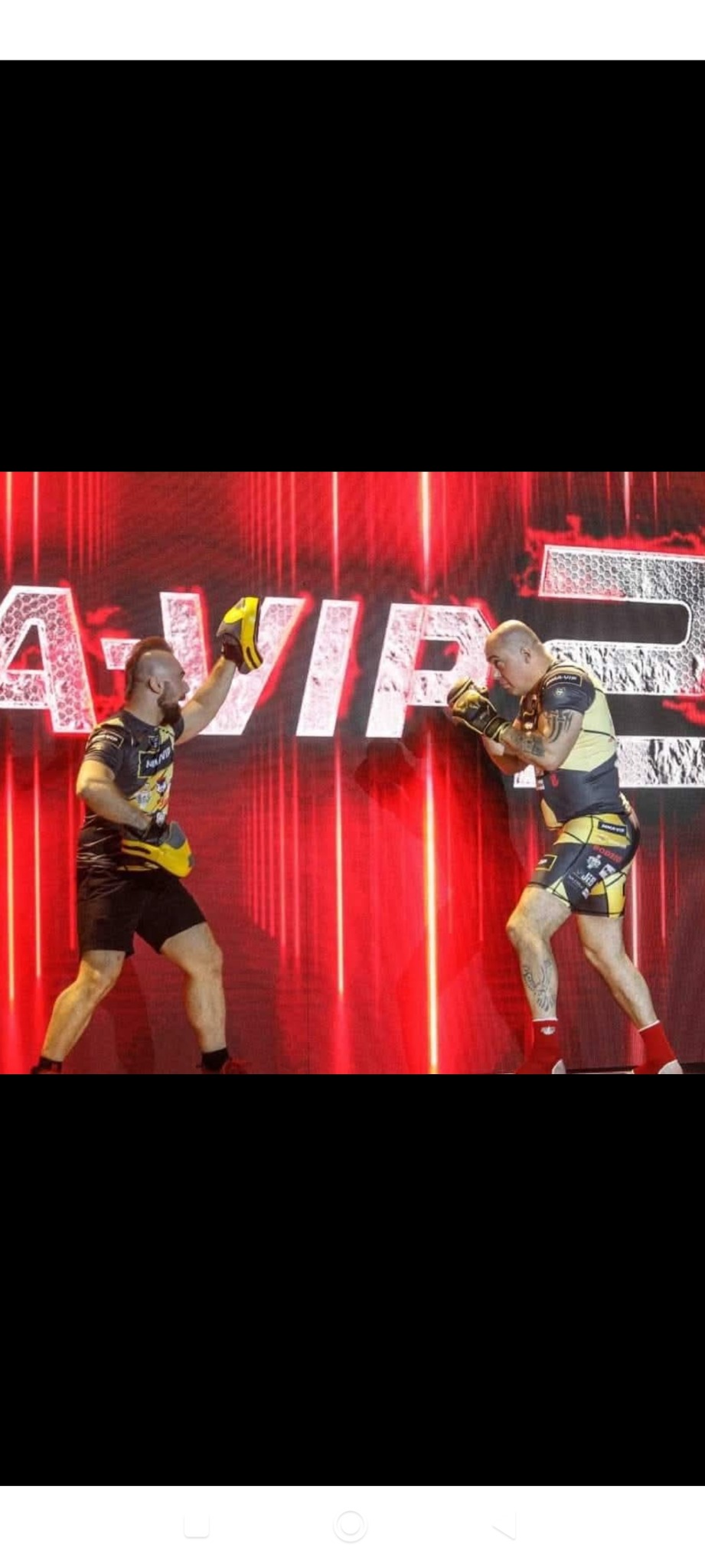 Dwóch zawodników sportów walki w rękawicach bokserskich podczas sparingu na tle czerwonej sceny z napisem VIP.