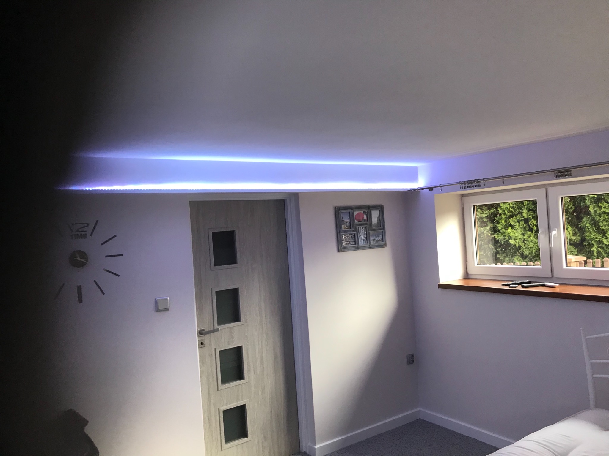 Pokój po remoncie z nowymi drzwiami z czterema szybkami, oświetleniem LED podsufitowym i oknem z widokiem na zieleń.