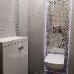 Nowoczesna toaleta podwieszana otoczona mozaiką z podświetleniem LED, obok zabudowa sanitarna i płytki ścienne z dekoracyjnym paskiem mozaiki, podłoga z ciemnego marmuru.