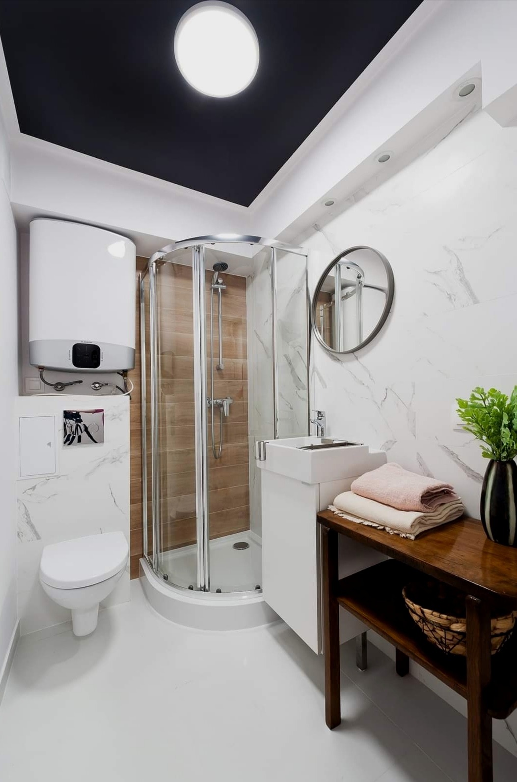 Nowoczesna łazienka z kabiną prysznicową narożną, białą umywalką nablatową, podgrzewaczem wody i czarnym sufitem podwieszanym z okrągłym oświetleniem.