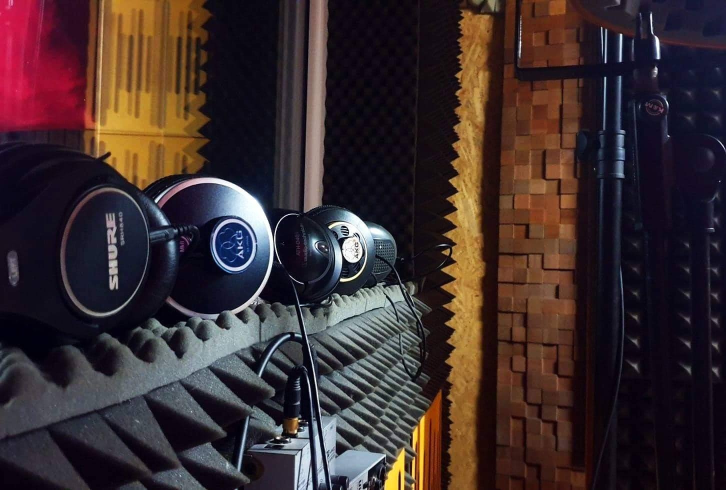 Rząd słuchawek studyjnych różnych marek (Shure, AKG, Audio-Technica) ułożonych na piankowych panelach akustycznych w profesjonalnym studiu nagrań, widoczne kable i sprzęt audio.