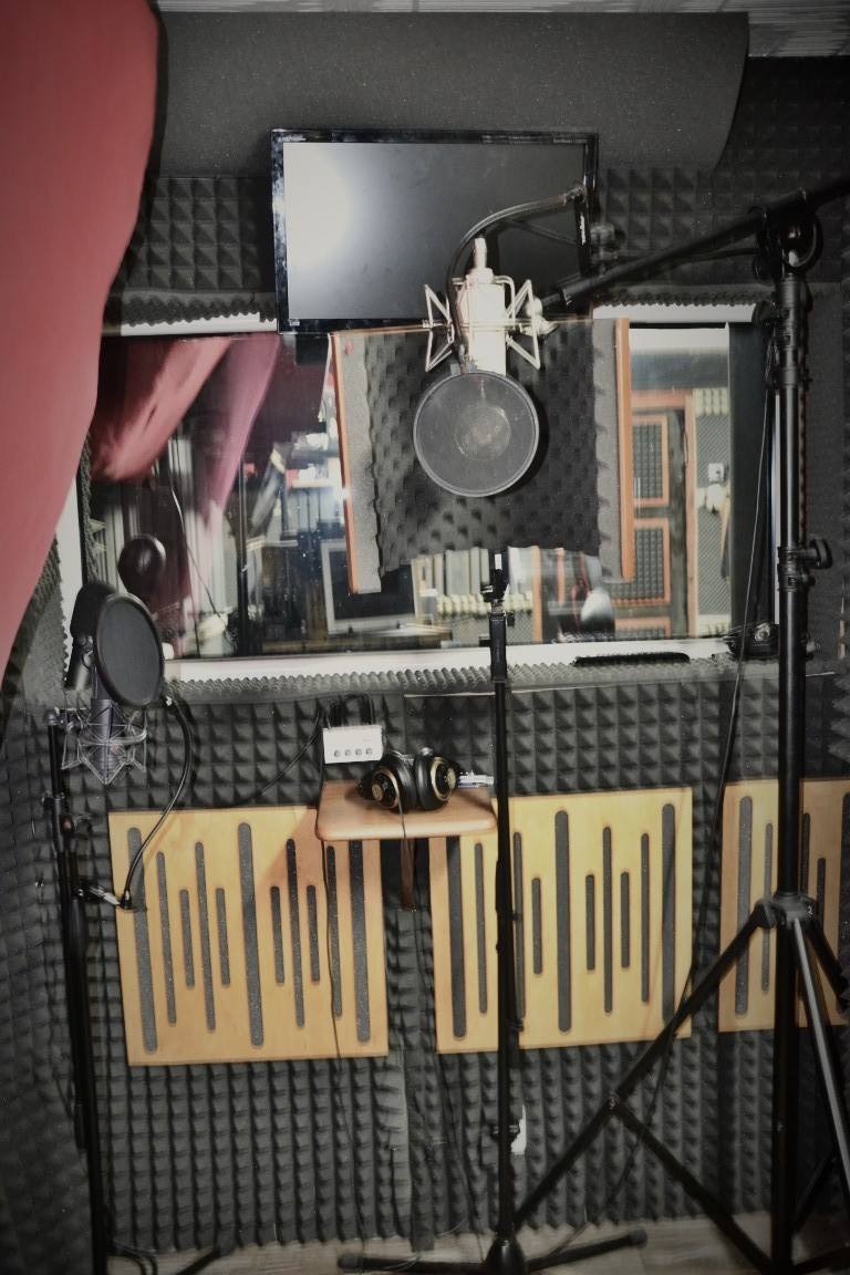 Wnętrze studia nagrań z mikrofonem studyjnym z pop filtrem, słuchawkami na małej półce i panelami akustycznymi na ścianach.