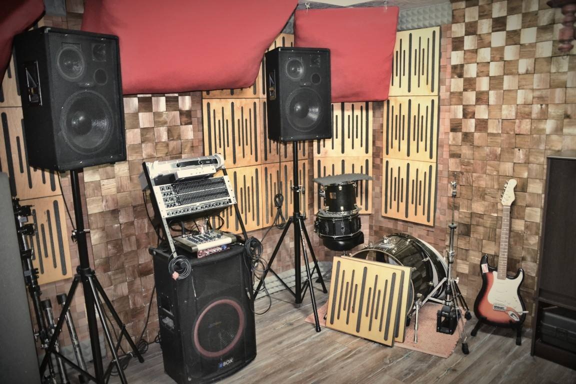 Wnętrze studia nagraniowego z panelami akustycznymi na ścianach, perkusją, gitarą elektryczną i mikserem dźwięku na statywie.