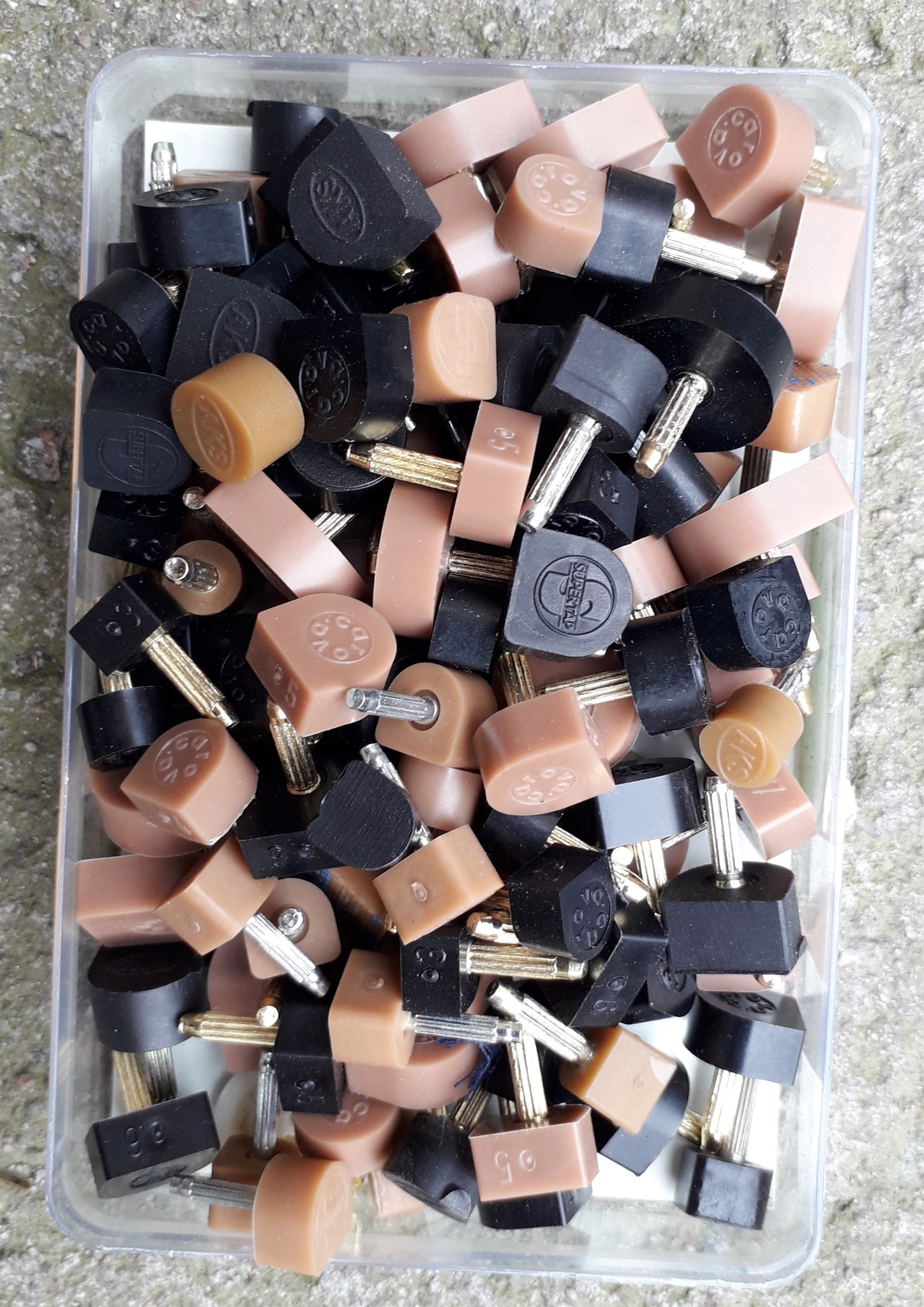Różne rodzaje obcasów do butów w plastikowym pojemniku, widoczne obcasy w kolorze czarnym i beżowym, niektóre z oznaczeniami rozmiarów.