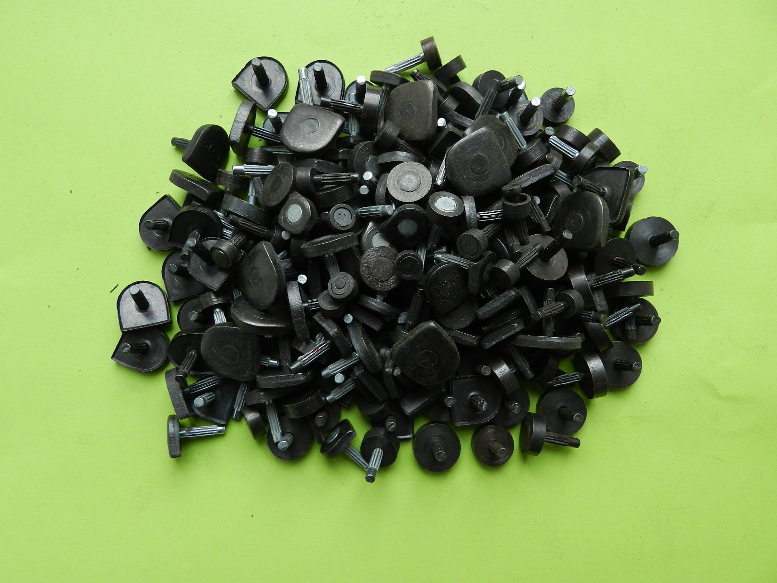Stos ciemnych, gumowych fleczków do butów z metalowymi trzpieniami na zielonym tle.