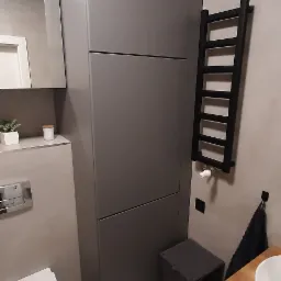 Nowoczesna łazienka w szarościach z wiszącą toaletą, grzejnikiem drabinkowym i szafką z umywalką na drewnianym blacie.