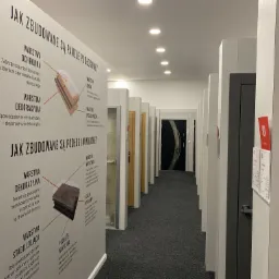 Wnętrze salonu ekspozycyjnego w Olsztynie z rzędem drzwi i paneli podłogowych, prezentujących przekroje warstw konstrukcyjnych na planszach informacyjnych.