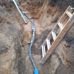 P.H.U. Dr Volt Zbigniew Frejman - Kabel w wykopie ziemnym, widoczne rury osłonowe, drabina drewniana. Przyłącze kablowe w trakcie realizacji, ziemia piaszczysta, brązowa.