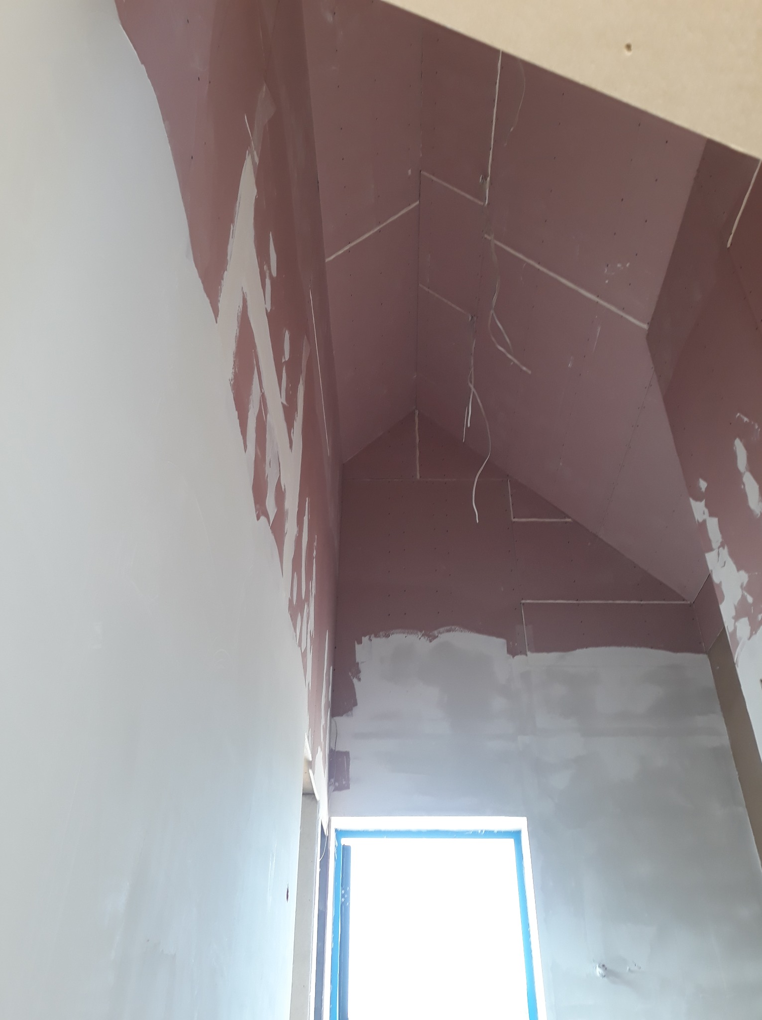 Poddasze po montażu płyt gipsowo-kartonowych i częściowym szpachlowaniu. Widoczne kable elektryczne zwisające z sufitu. Okno zabezpieczone folią.