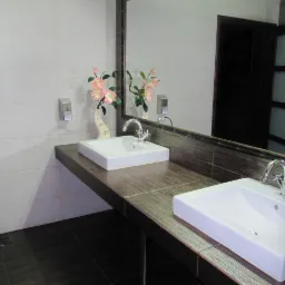 Nowoczesna łazienka z dwiema białymi umywalkami na blacie z płytek imitujących drewno, lustro z kwiatami i ciemne płytki podłogowe.