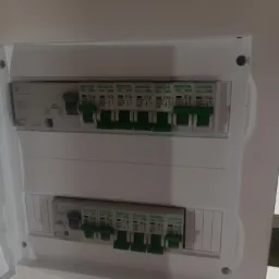 Otwarta, biała skrzynka rozdzielcza z widocznymi bezpiecznikami Gacia, z których część jest w pozycji włączonej (dźwignie w dół), a część wyłączona (dźwignie w górę).