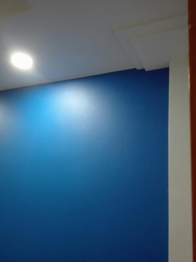 Świeżo pomalowana na niebiesko ściana z widocznym oświetleniem sufitowym i białymi dekoracjami narożnymi.