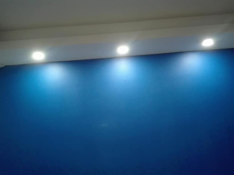 Ściana w intensywnym odcieniu niebieskiego, oświetlona trzema punktowymi lampami sufitowymi w Krakowie. Widoczna gładka powierzchnia ściany i równomierne rozprowadzenie światła.