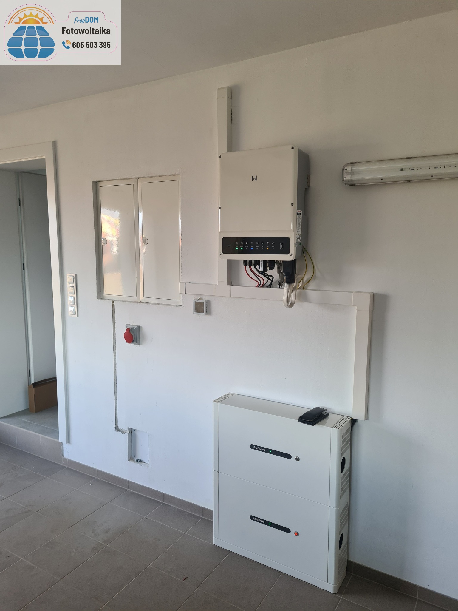 Biały inwerter i dwuczęściowy akumulator energii GoodWe zamontowane na ścianie w pomieszczeniu. Widoczne przewody i instalacja elektryczna.
