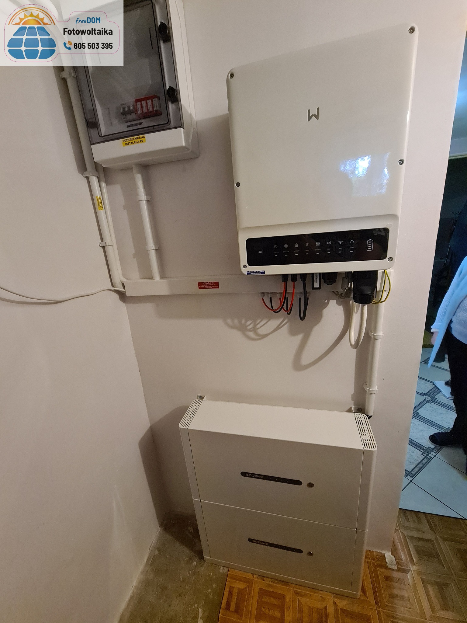 Wnętrze z zamontowanym inwerterem i magazynem energii GoodWe na ścianie, widoczne okablowanie i skrzynka rozdzielcza AC. Instalacja w pomieszczeniu.