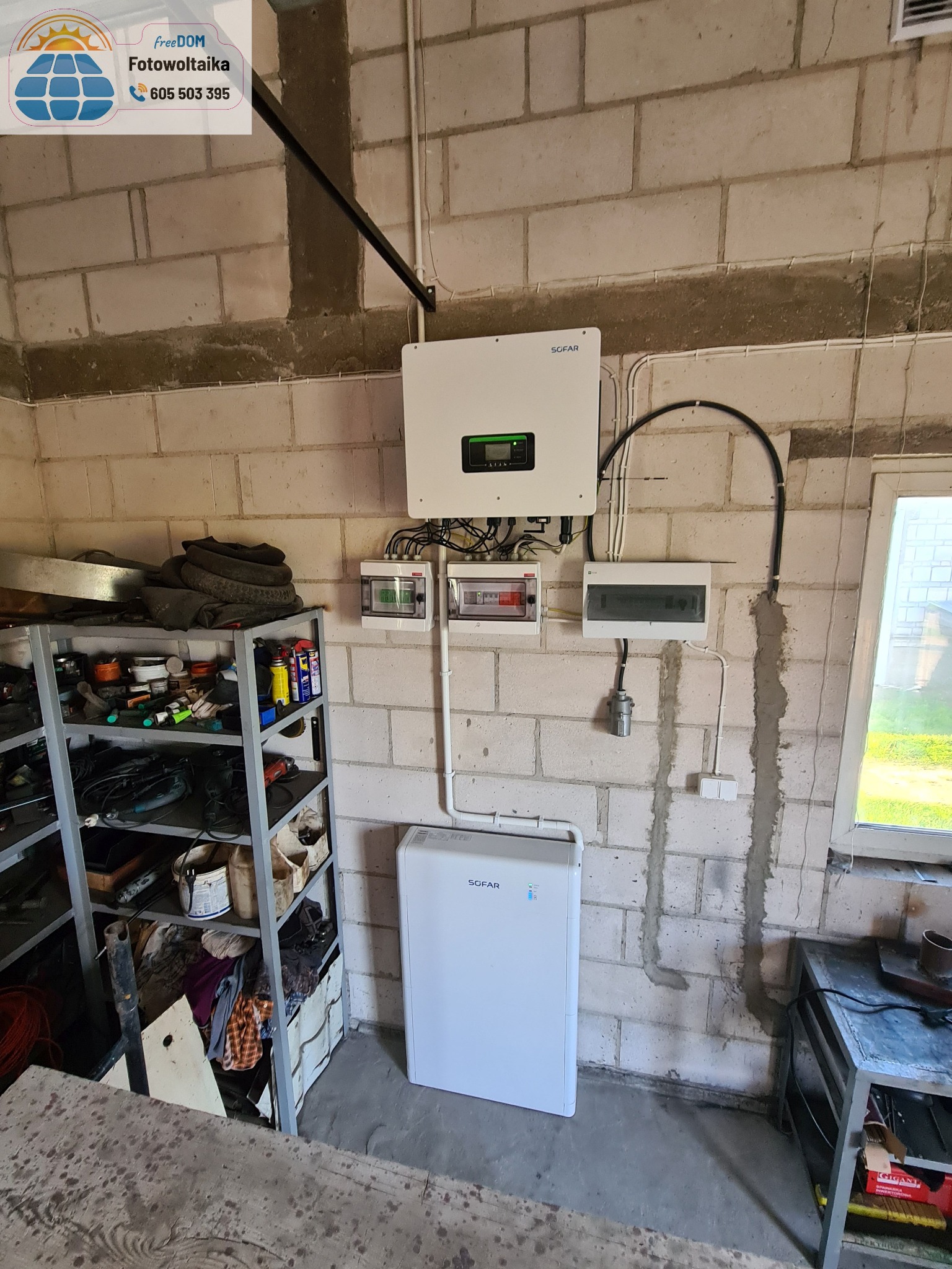 Instalacja SOFAR: inwerter, rozdzielnice i magazyn energii w surowym garażu z betonowych bloków. Widoczne okablowanie i metalowy regał z narzędziami.