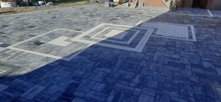 Ułożona kostka brukowa w odcieniach szarości i błękitu, z dekoracyjnymi wzorami w kształcie kwadratów z jasnych kostek, częściowo zacieniona.