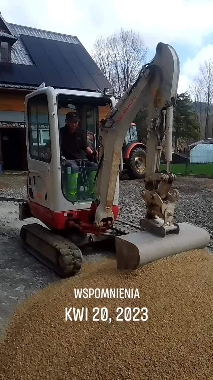 Mini koparka Takeuchi rozładowuje żwir na podjazd w słoneczny dzień, w tle dom z panelami słonecznymi na dachu.