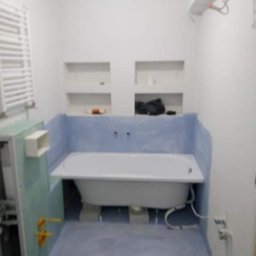 Kamant - Biała wanna częściowo obudowana, z widocznymi instalacjami, w surowym wnętrzu łazienki z przygotowanymi niszami w ścianie, przed wykończeniem.